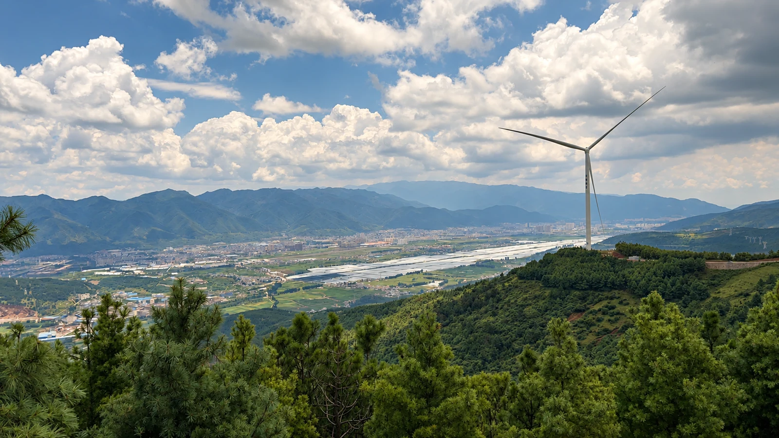 Yunnan agricultural valley with forested slopes, clouds and a wind turbine